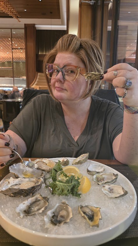Renee Shupe at a restaurant table, holding up an oyster with a playful look